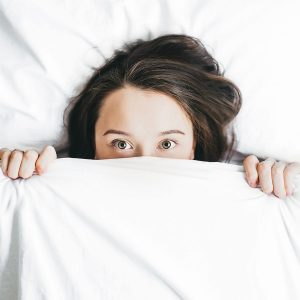 Lady scared and lying in bed hiding under covers